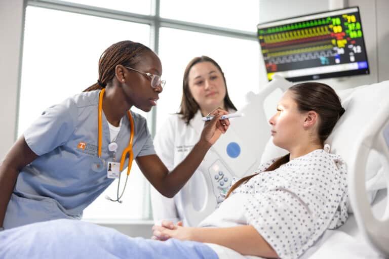 A nursing student examines a patient in a hospital bed.